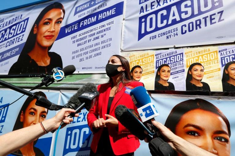 U.S. Rep. Alexandria Ocasio-Cortez, speaks to members of the media while standing beside a truck plastered with campaign posters after greeting voters in Astoria, Queens on Jun. 23, 2020, on primary election day in New York. (CP/AP/Kathy Willens)