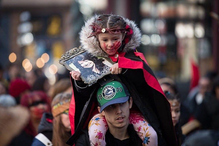 Sofia Mitchell-Schiewe holds a photo of her late grandmother Francis Mitchell while sitting on her father James Schiewe's shoulders during the annual Women's Memorial March in Vancouver, on Feb. 14, 2020 (Darryl Dyck/CP)
