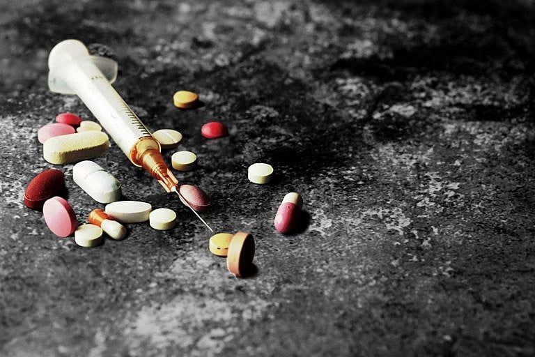 A picture of a needle and some pills on the ground