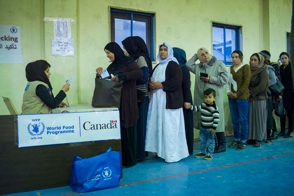 Residents of the Duhok Camp line up to receive aid. Rather than hand out baskets of food as in the past, refugees are given cash to buy their own food. The result: local markets have recovered quickly, benefiting the local economy. (Photo by Peter Bregg) 