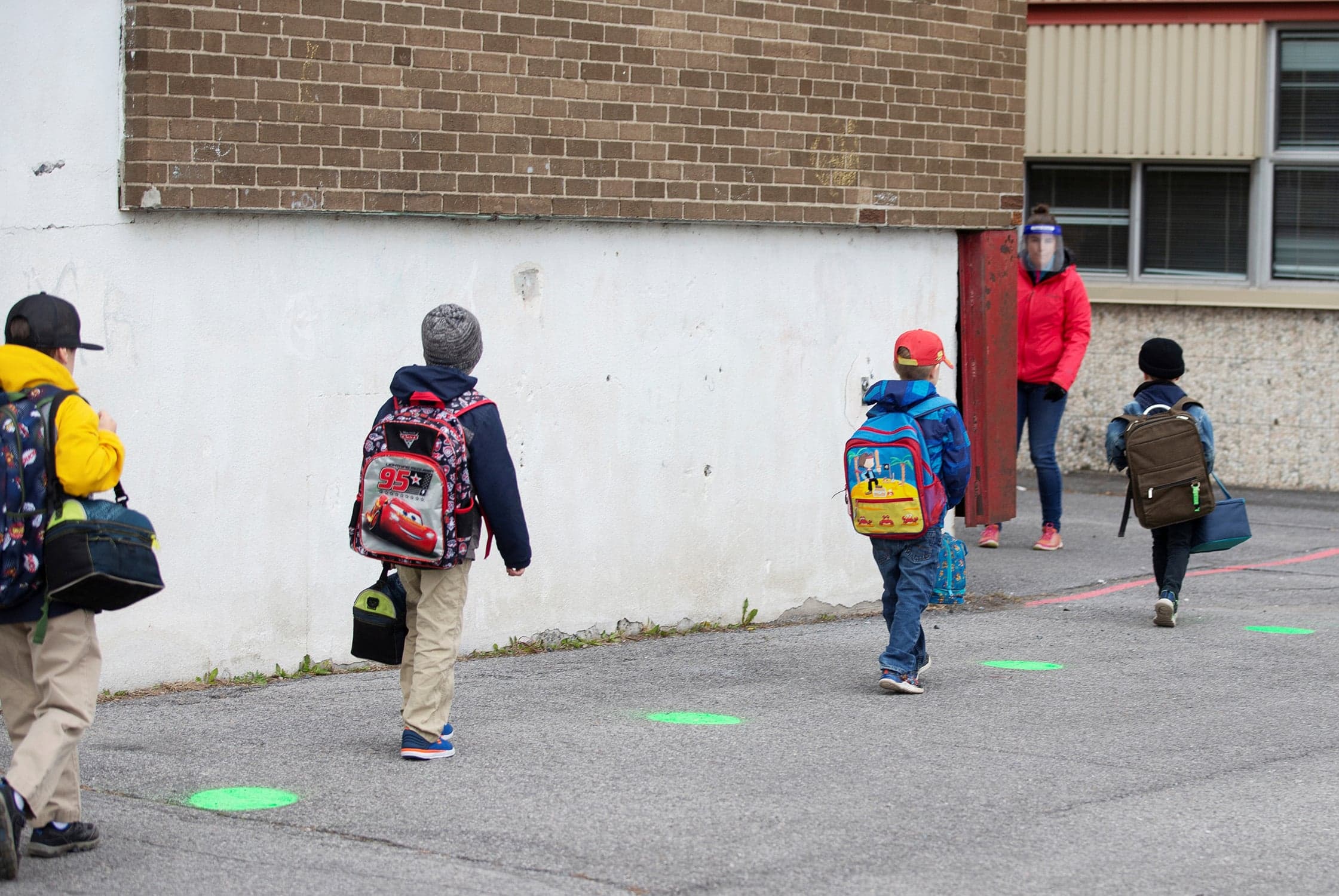 Children in Saint-Jean-sur-Richelieu, Que., use green dots painted on the tarmac to help maintain proper social distancing; schools outside the greater Montreal area began to reopen in mid-May as the COVID-19 pandemic wore on, and children were asked to adapt to new realities (Christinne Muschi/Reuters)