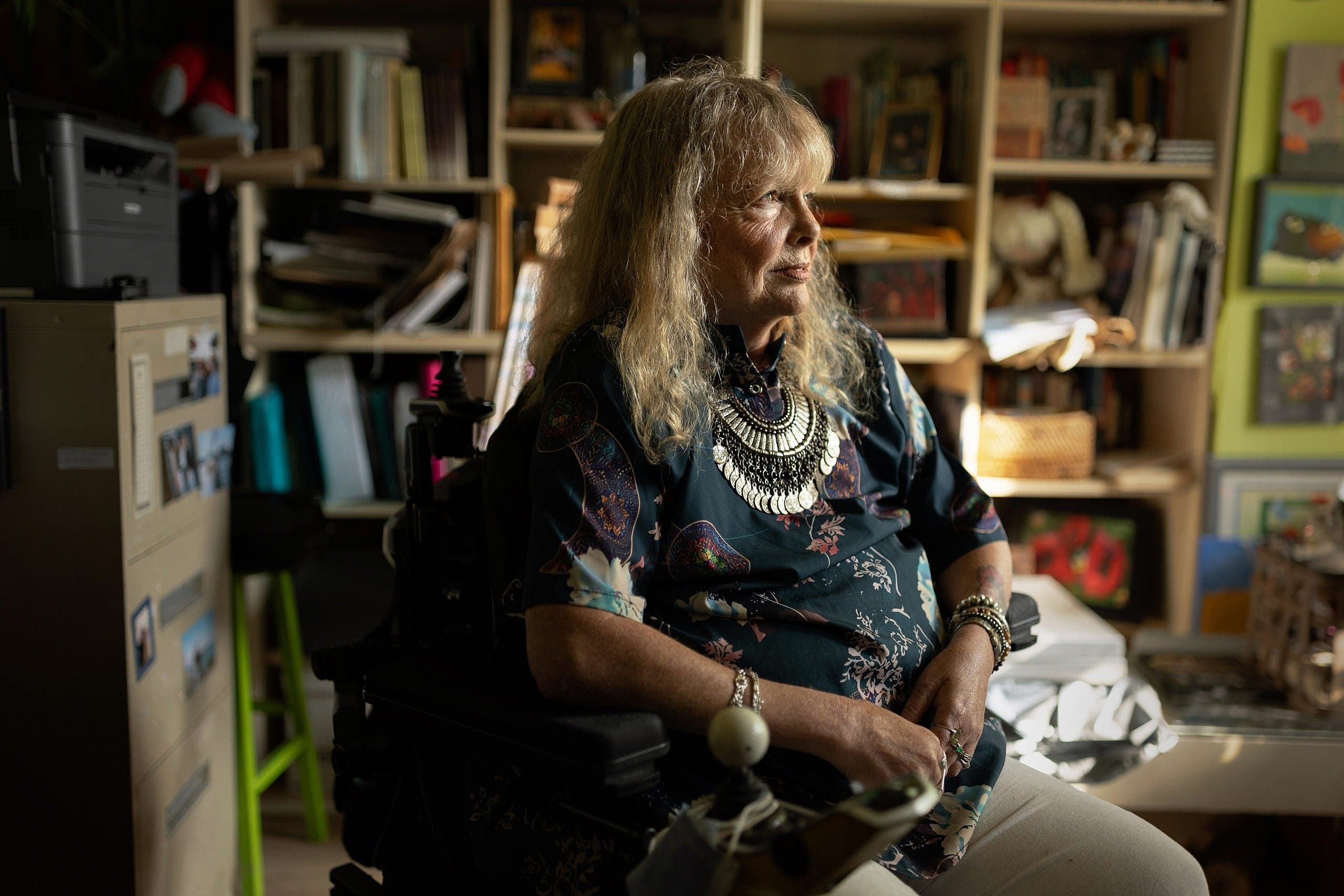 woman with blonder shoulder length hair sitting in a wheelchair and faced away from the camera
