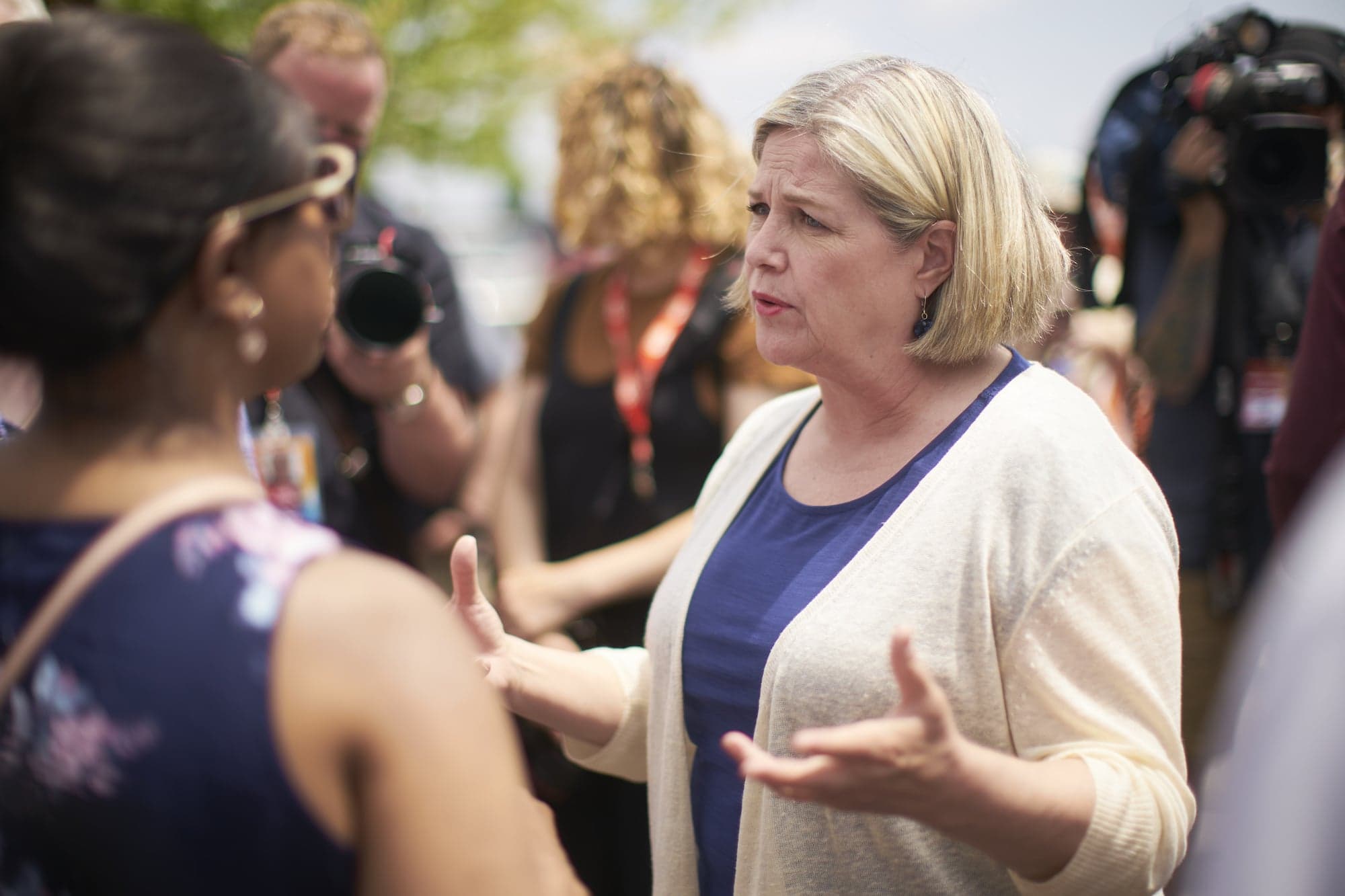 A woman speaks to a crowd of people on a sunny day