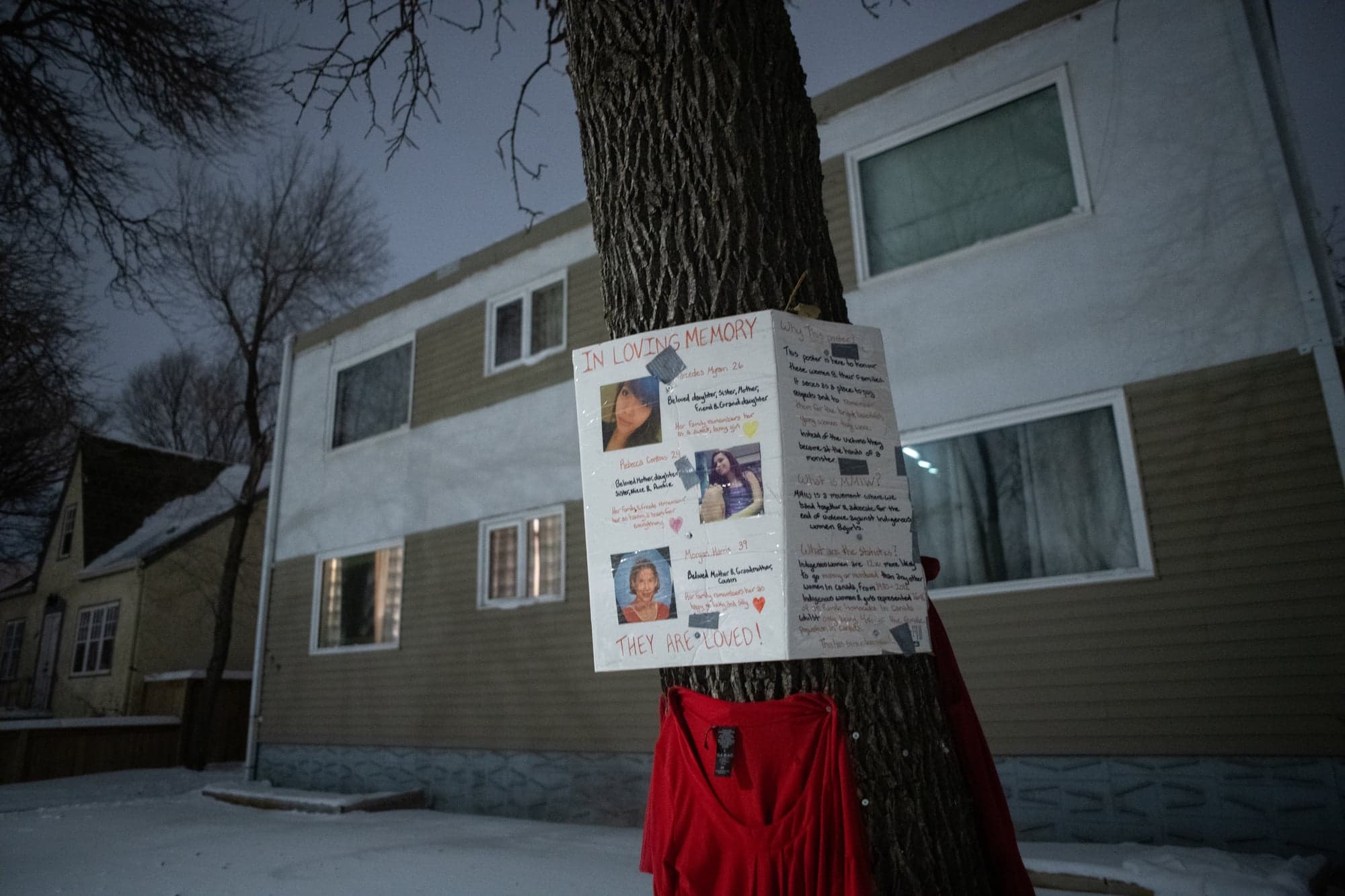 A picture of a makeshift "IN LOVING MEMORY" memorial, with the victims' faces printed out and taped to a piece of white cardboard.
