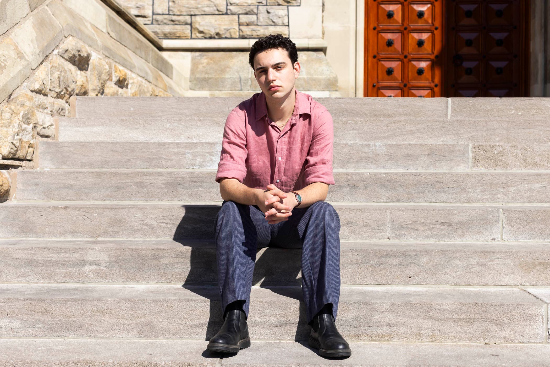 A young man sitting on the steps of a university building