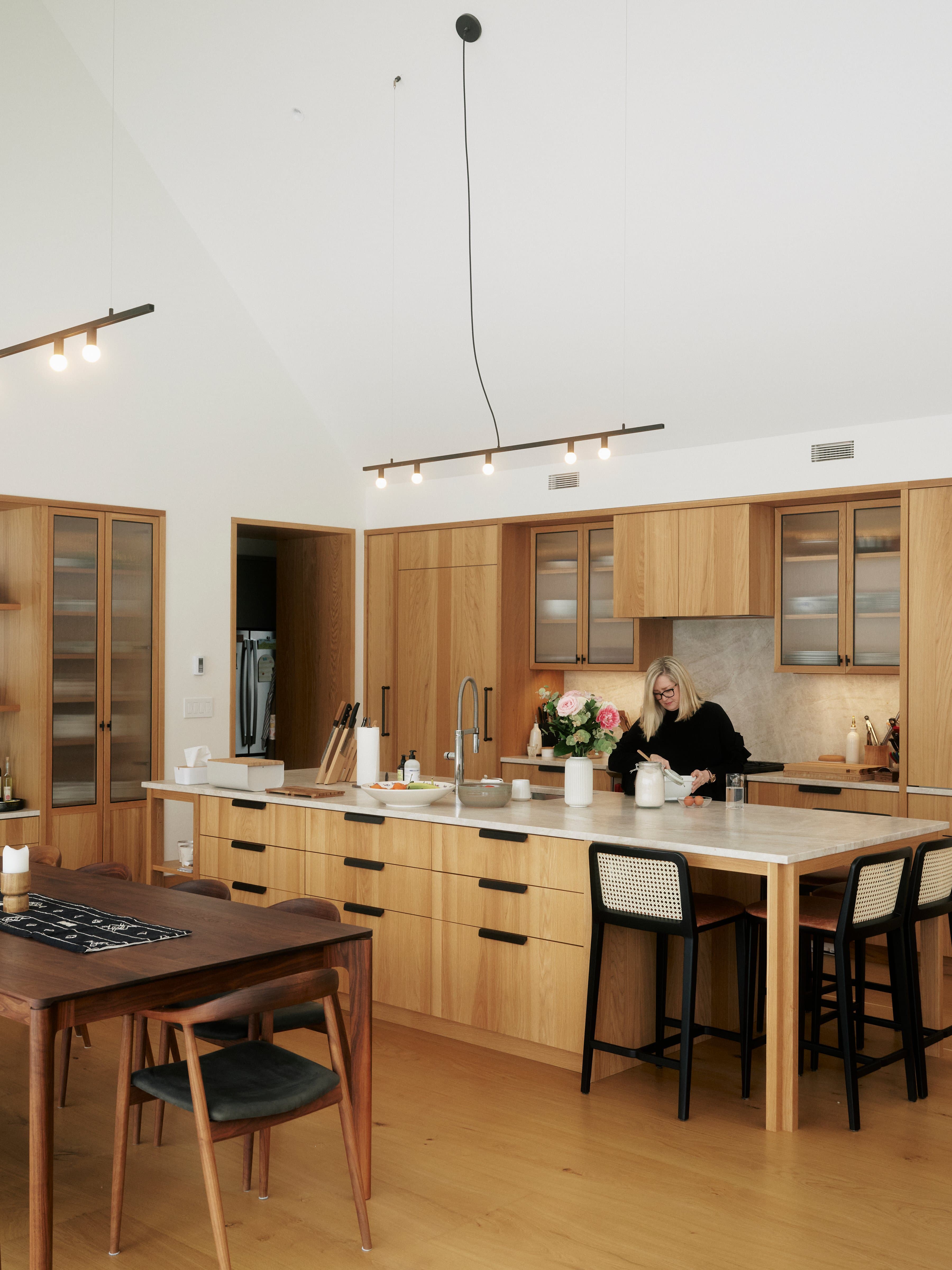 A kitchen with white cathedral ceilings, wood cabinetry and a large island with drawers and a stone countertop