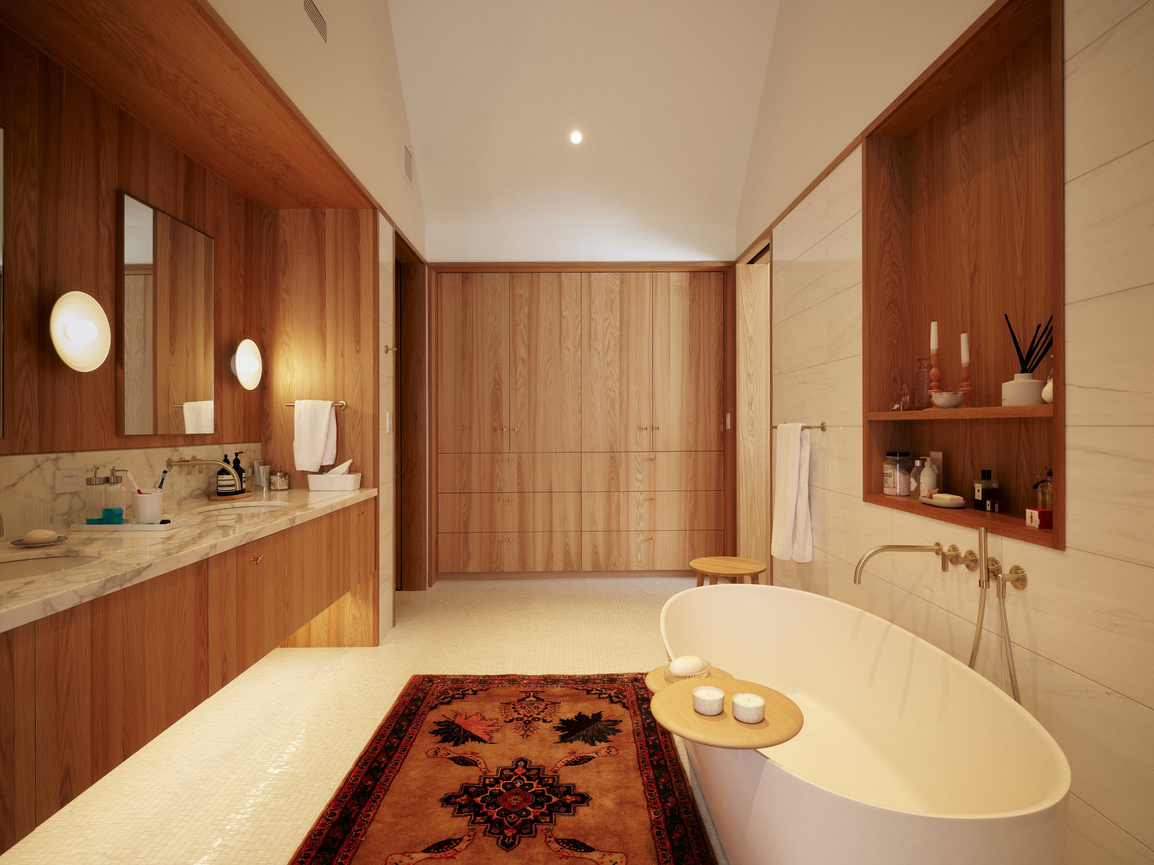 A large bathroom with high ceilings built-in cabinets and a marble wall behind the bathtub