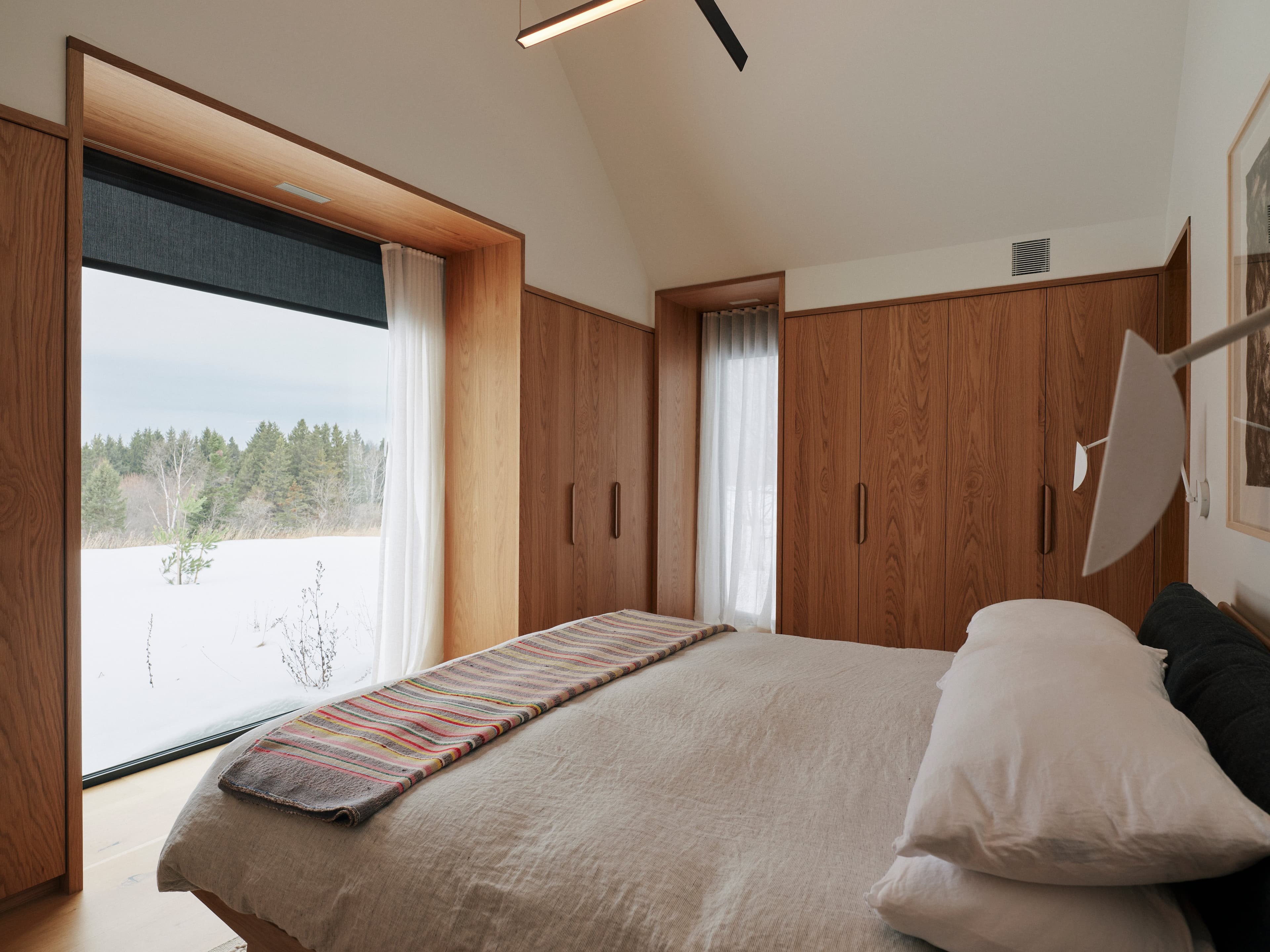 A wood-panelled bedroom with two large windows and cathedral ceilings
