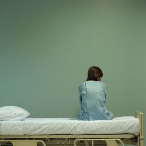 Female patient sitting on hospital bed, rear view