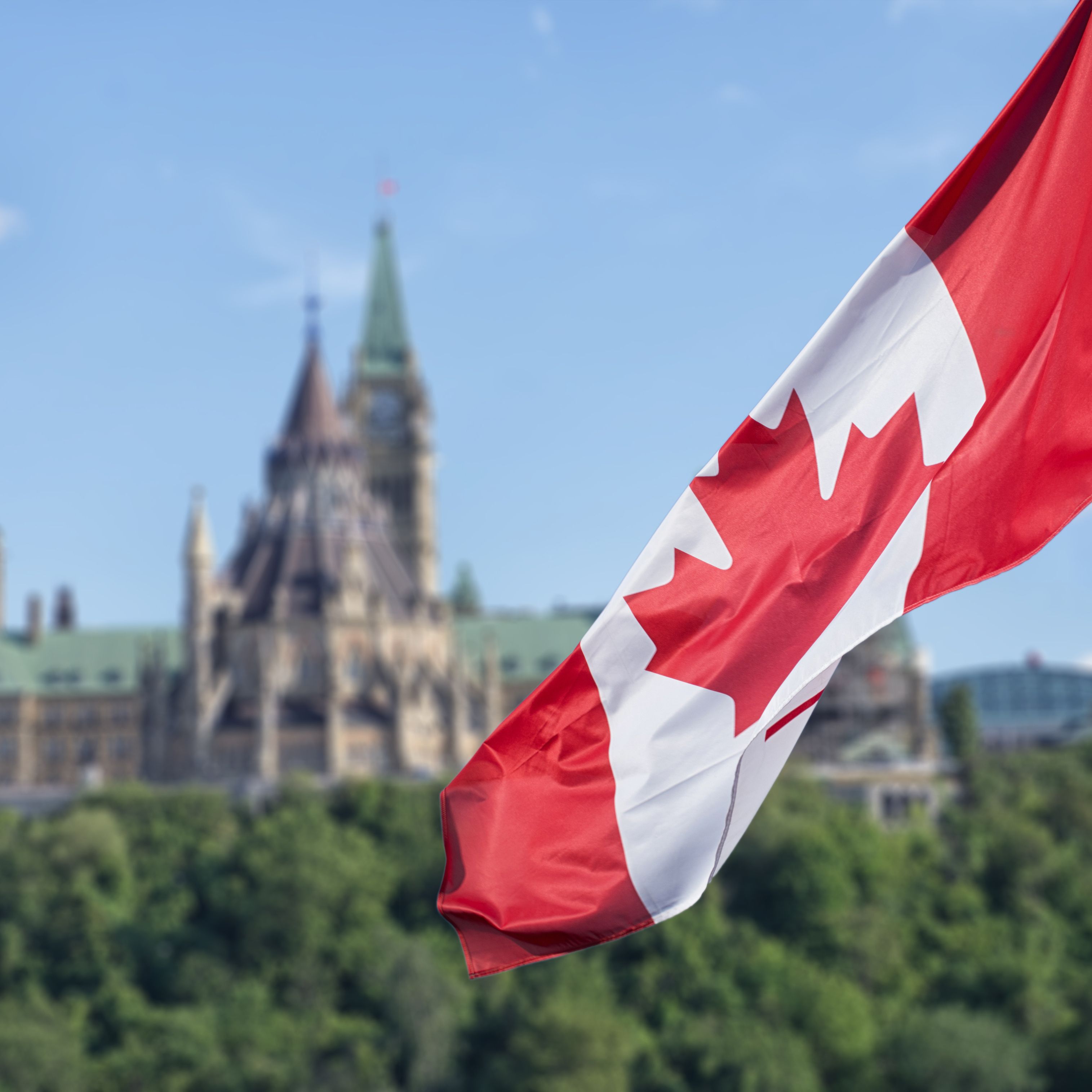 Canadian flag waving with Parliament Buildings hill and Library
