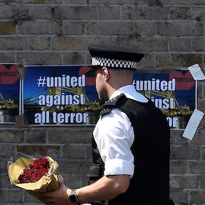 A police officer carries flowers to leave alongside of messages near to where a van was driven at muslims in Finsbury Park, North London