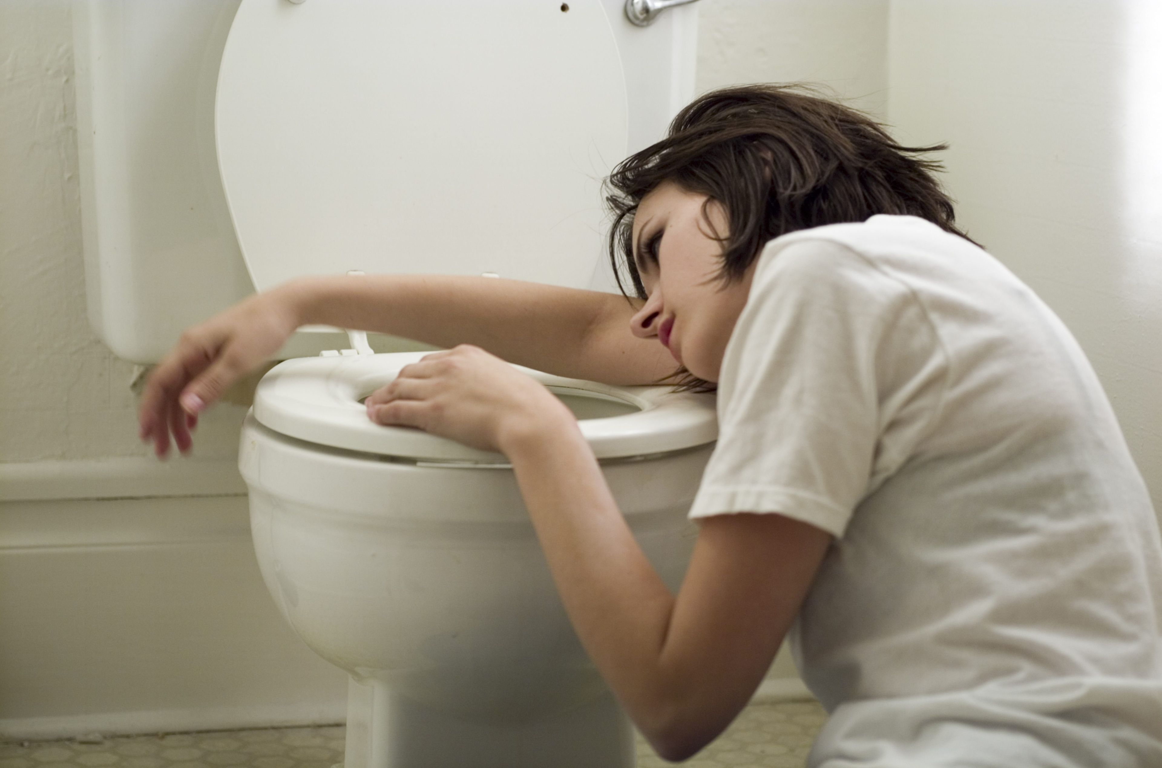 Sick young woman leaning on toilet bowl