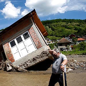 A man reacts near a house tilted by floods in the village of Krupanj