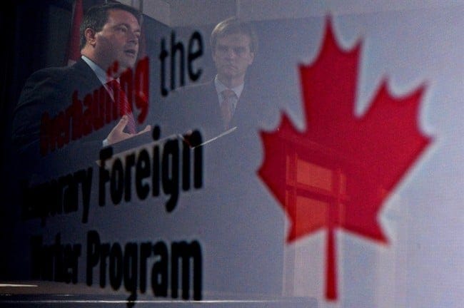 Employment Minister Jason Kenney, left, and Immigration Minister Chris Alexander are seen in a reflection at a news conference in Ottawa on Friday, June 20, 2014 on reforms to the Temporary Foreign Worker Program. (Sean Kilpatrick/The Canadian Press)
