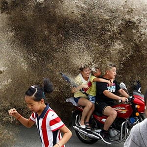 Visitors run away as waves caused by a tidal bore surge past a barrier on the banks of Qiantang River, in Hangzhou