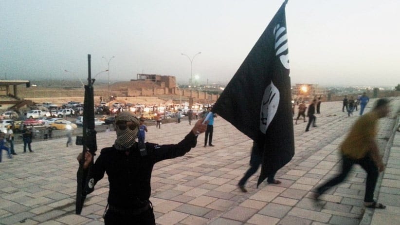 A fighter of the ISIL holds a flag and a weapon on a street in Mosul