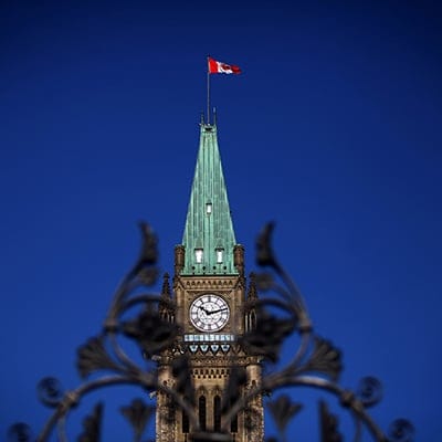 The Canadian flag flies above Parliament Hill in Ottawa, Ontario, Canada, on Tuesday, Feb. 11, 2014. Canadian Finance Minister Jim Flaherty ramped up efforts to return the country to surplus in a budget that raises taxes on cigarettes and cuts benefits to retired government workers while providing more aid for carmakers. Photographer: Cole Burston/Bloomberg via Getty Images