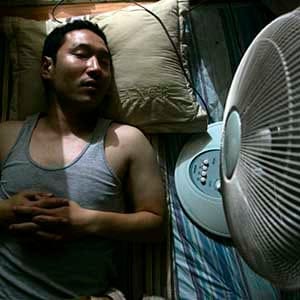 A man lies next to an electric fan in his home in Seoul July 4, 2007. Summertime in South Korea means cold beer on steamy nights and lonely deaths in stuffy rooms blamed on electic fans. Electric fans and Koreans are a deadly combination, according to an urban legend in the country that has it if a person sleeps in a closed room with a fan on all night they may never wake up. To match feature KOREA-FANS/  REUTERS/Han Jae-Ho (SOUTH KOREA) - RTR1RK3N