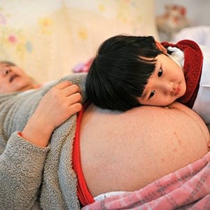 Li Yan (L), pregnant with her second child, lies on a bed as her daughter places her head on her mother's stomach in Hefei, Anhui province February 20, 2014. Li gave birth to a baby boy on February 23, 2014 after Li's family became the first to receive a birth permit to have a second child in the province earlier this month, local media reported. Chinese government said late last year it would allow millions of families to have two children, with a relaxation of its one-child policy if one of the parents was an only child. Picture taken February 20, 2014. REUTERS/China Daily (CHINA - Tags: SOCIETY POLITICS) CHINA OUT. NO COMMERCIAL OR EDITORIAL SALES IN CHINA - RTR3FP4Z