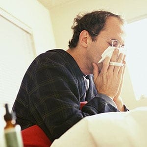 Man sick in bed blowing his nose.  Marc Romanelli/Getty Images