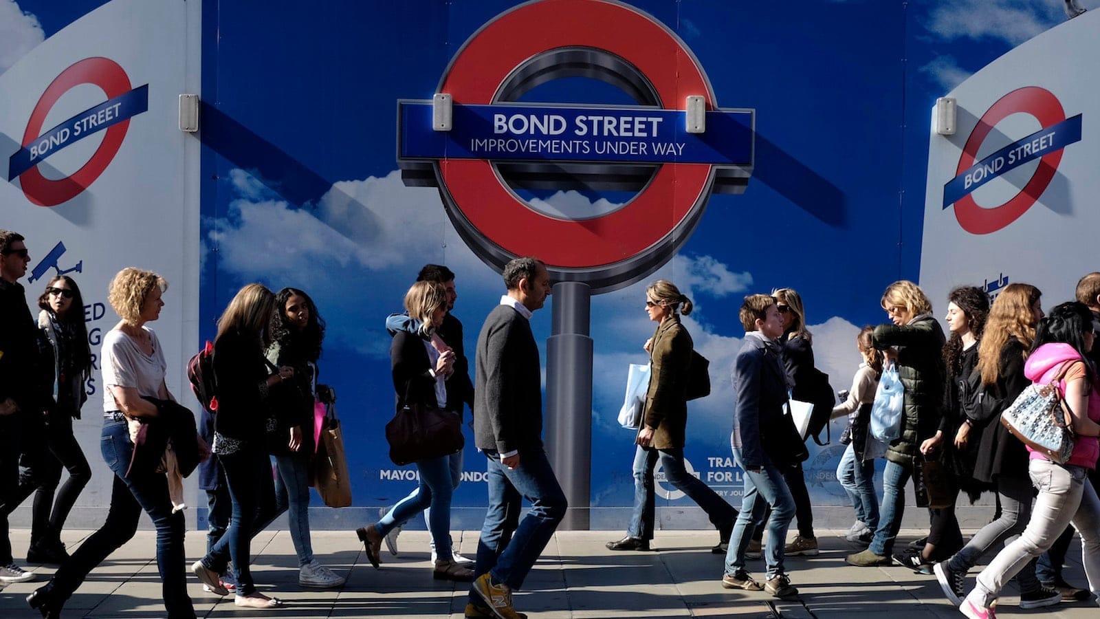 People walk past signs for a London Underground improvement programme during a busy afternoon on Oxford Street in London. 