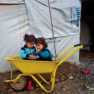 © Mohammad Husein, 15 years old when the workshops began. Syrian Refugee Camp, Kawergosk, Kurdistan, Iraq. 
Photograph created as part of the five-year project Exile Voices, launched in December 2013 by Reza to train refugee children in the camps in photography.
Mohammad Husein, aged 17, captures two little girls playing in a wheelbarrow at the Kawergosk refugee camp. Despite adversity, children continue to play and live.