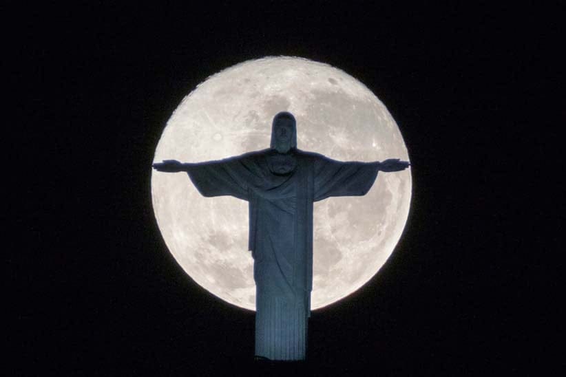 The silhouette of the statue of Christ the Redeemer stands out against the full moon in Rio de Janeiro; the city needs all the prayers it can get in advance of the Summer Olympics (Yasuyoshi Chiba/AFP/Getty Images)
