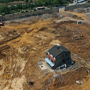 One of nail houses surrounded with land lowed down for meters stands on the construction site on March 30, 2013 in Yichang, Hubei province of China. The owners of nail houses didn't reach an agreement with property developer on relocation compensation one year ago. After that, water and electricity systems of nail houses were broke by strangers frequently and purposely. Nowadays, land surround of the two buildings have been diged by property developer for several meters so that the two houses are like two nails in the construction site.  (VCG/Getty Images)