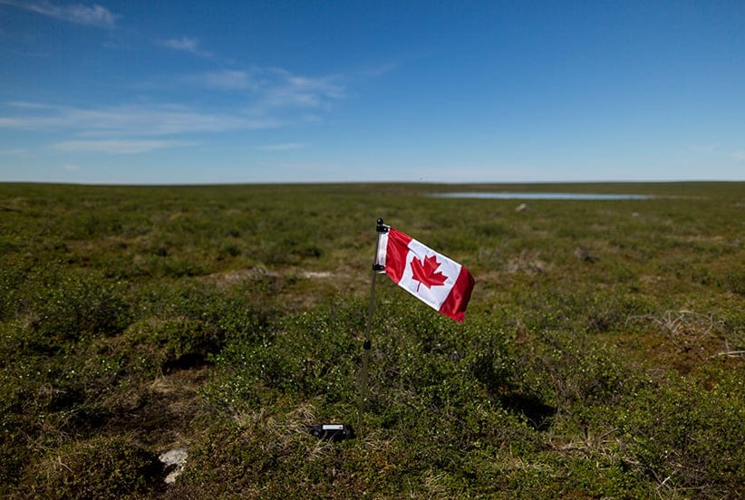 Meagan Campbell plants a flag and leaves a geocache at the exact centre of Canada in Nunavut, Canada. (Photograph by Nick Iwanyshyn)