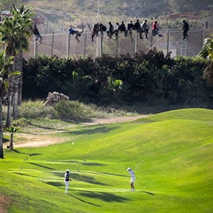 A golfer hits a tee shot as African migrants sit atop a border fence during an attempt to cross into Spanish territories between Morocco and Spain's north African enclave of Melilla October 22, 2014. Around 400 migrants attempted to cross the border into Spain, according to local media. Picture taken October 22, 2014. (Jose Palazon/Reuters)