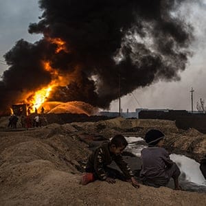 Young boys watch on as firefighters work to extinguish an oil well set on fire by fleeing ISIS members on November 9, 2016 in Al Qayyarah, Iraq. Many families have begun returning to their homes in recently liberated towns south of Mosul. Oil wells in the area that were set on fire by ISIS continue to burn blanketing the area in think clouds of smoke and oil.  (Chris McGrath/Getty Images)