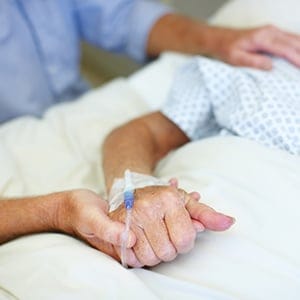 Closeup shot of an elderly man holding his wife's hand while she is ill in the hospital. (Squaredpixels/Getty Images)