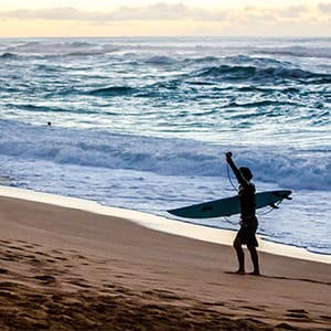 Surfer carrying surfboard comes in after surfing large waves at Sunset Beach famous for big surf and golden sunsets. Located on the North Shore of Hawaii on the tropical travel destination Island of Oahu. (Julie Thurston Photography/Getty Images)