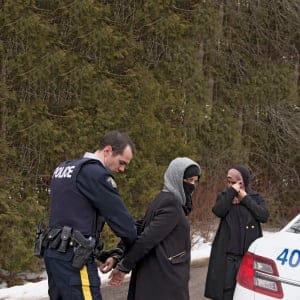 Two women claiming to be from Yemen are detained by a Royal Canadian Mounted Police (RCMP) officer after crossing the U.S.-Canada border into Hemmingford, Quebec on February 22, 2017.  (Christinne Muschi/Reuters)