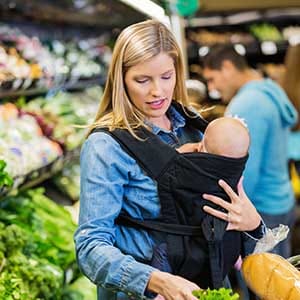 Mid adult Caucasian woman is shopping in grocery store or supermarket produce section with infant daughter. Young mother is wearing her baby in an infant carrier, and selecting healthy fruits and vegetables to purchase for family. (asiseeit)