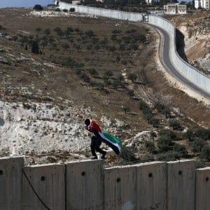 A Palestinian covered with national flag walks on top of the Israeli controversial separation wall separating the West Bank city of Abu Dis from east Jerusalem, during clashes with Israeli security forces, on November 2, 2015. (Ahmad Gharabli/AFP/Getty Images)