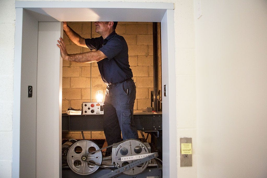Joe Leone, an Elevator Technician with Elevator One, looks inside an elevator shaft while standing on top of the elevator during a routine elevator maintenance appointment. (Photograph by Della Rollins)