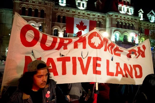 People hold up a sign during a demonstration on Parliament Hill, as a crowd gathered to erect a teepee as part of a four-day Canada Day protest, in Ottawa on Thursday, June 29, 2017. THE CANADIAN PRESS/Justin Tang