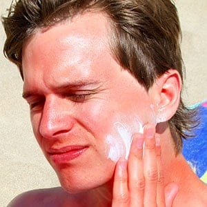 Sunburnt adult male applies sun lotion to face on beach, while lying on beach towel. (Tom And Steve/Getty Images)