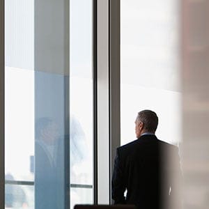 Businessman looking out conference room window. (Tom Merton/Getty Images)