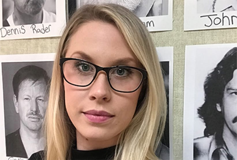 Sasha Reid stands before a board of photos  of prolific serial killers in her office at the University of Toronto (Photo: Courtesty of Sasha Reid) 