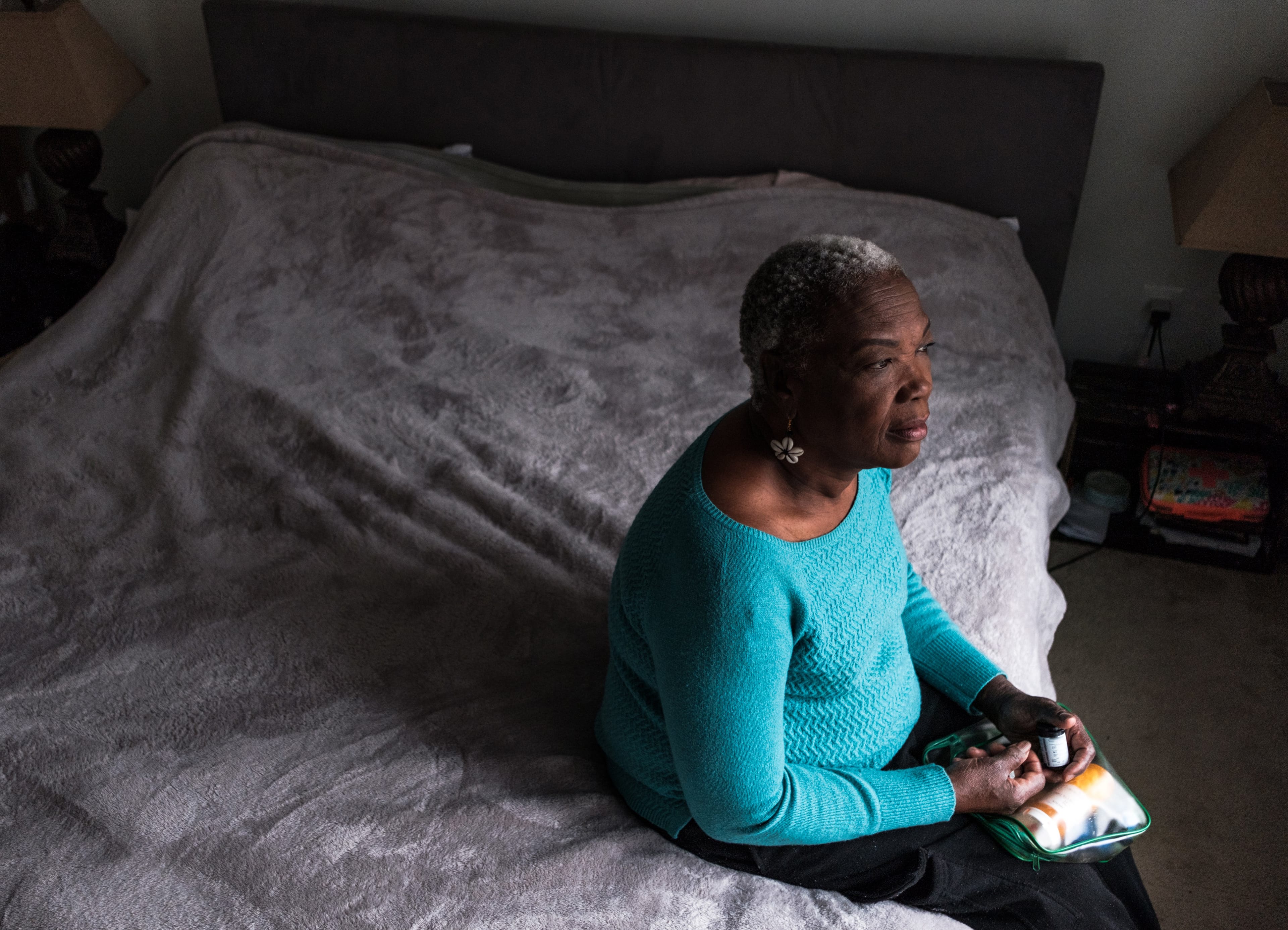 Elderly Haitian American woman sitting on a bed looking out the window while getting her glucose reader to check her blood sugar and insulin pen ready. (Eddie Pearson/Stocksy)