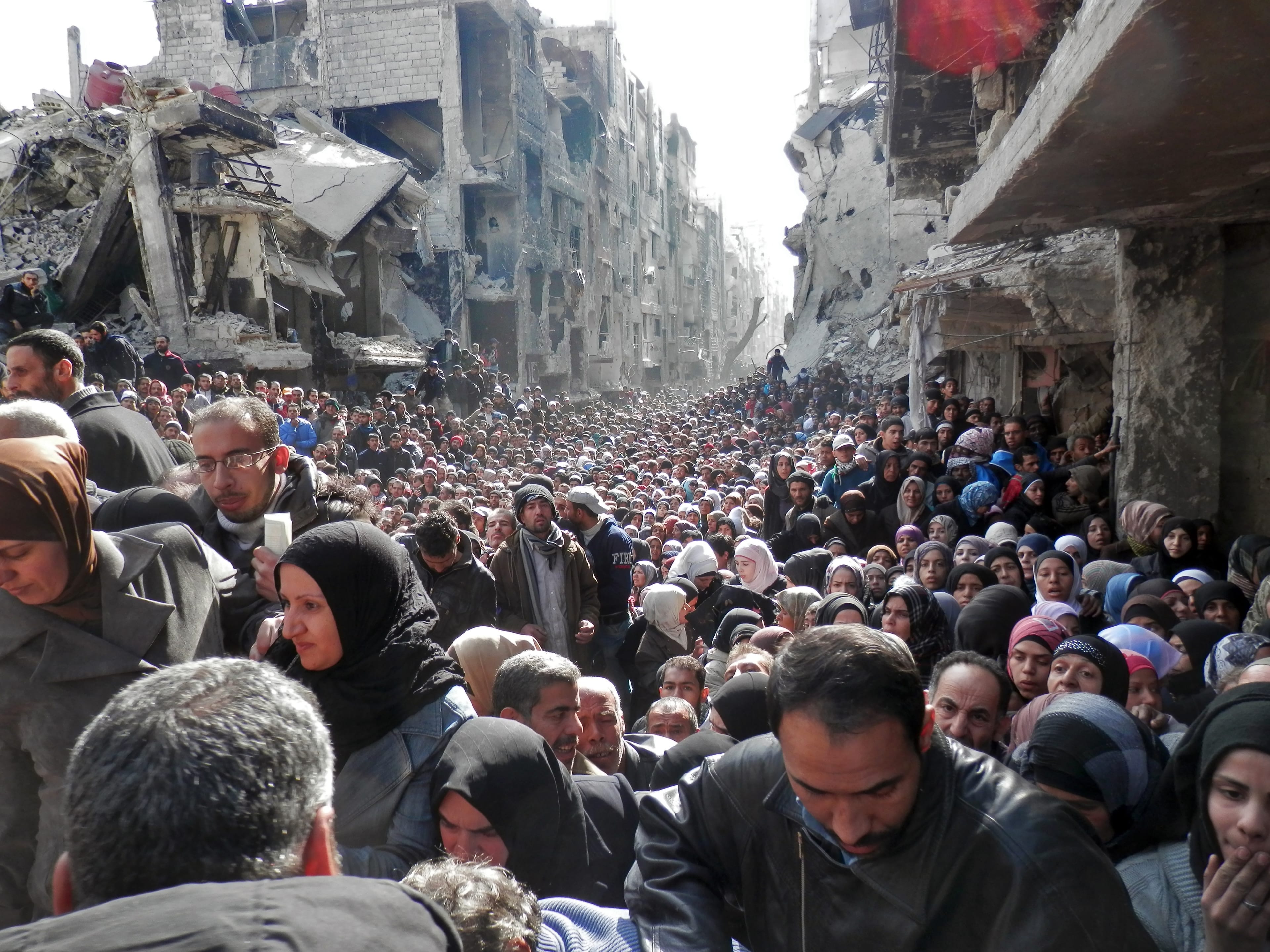 In this handout provided by the United Nation Relief and Works Agency (UNRWA), residents wait in line to receive food aid distributed in the Yarmouk refugee camp on January 31, 2014 in Damascus, Syria.  (Photo by United Nation Relief and Works Agency via Getty Images)