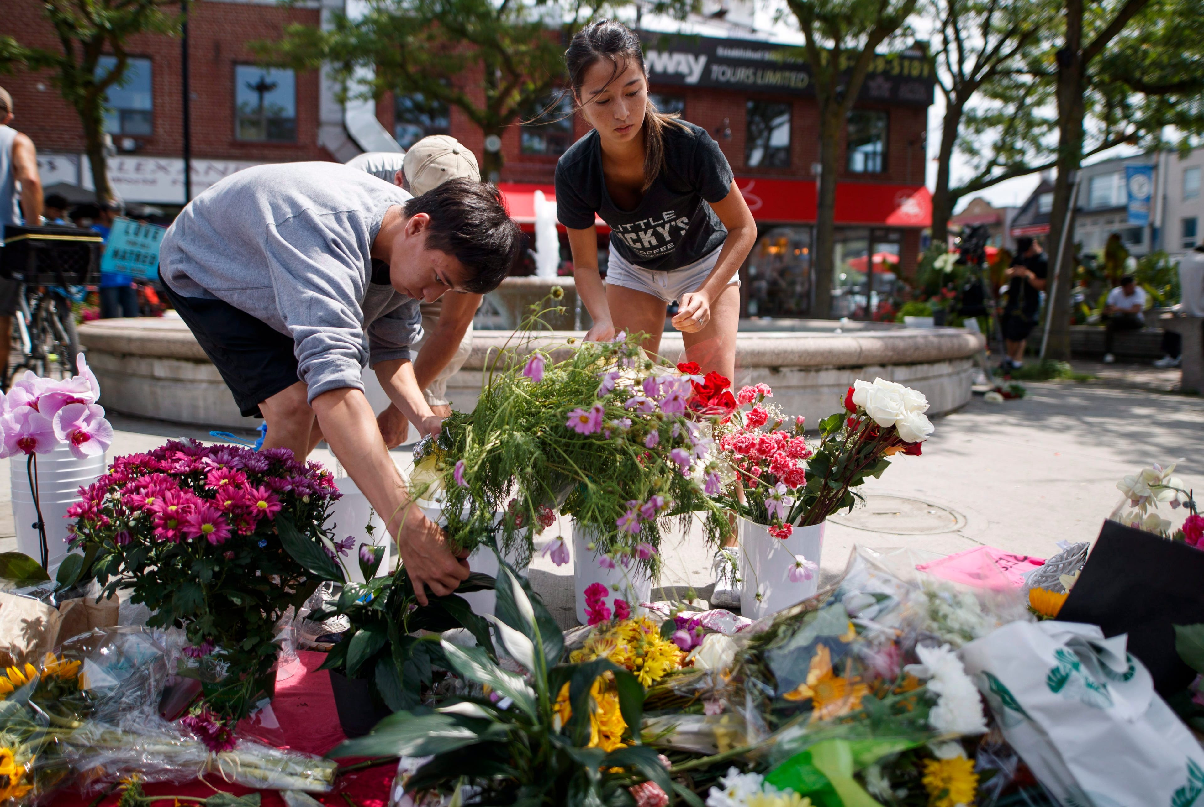 Kaya Malcolmson, right, and Jowa Malcolmson, left, organize flowers at a memorial site remembering the victims of a shooting on Sunday evening on Danforth Ave., in Toronto. (THE CANADIAN PRESS/Mark Blinch)