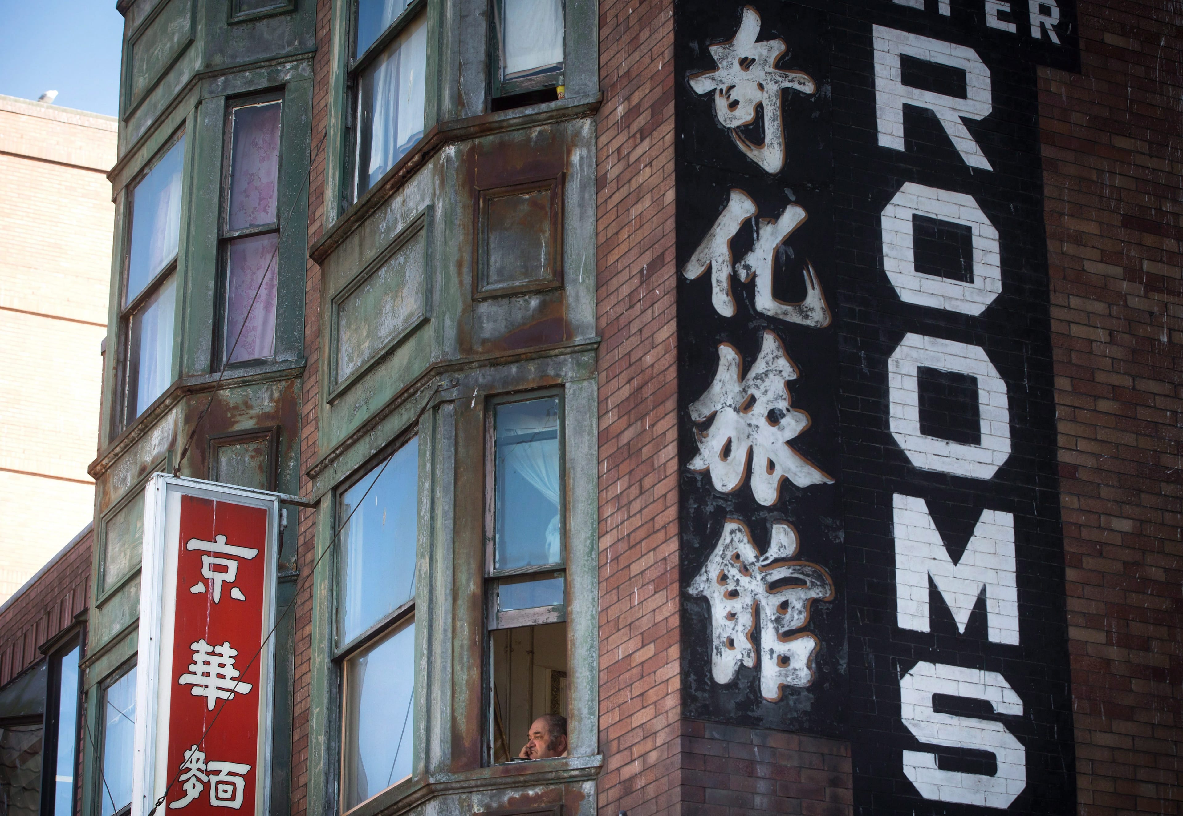 An elderly man looks out from an upper floor window at a single-room occupancy (SRO) hotel in Chinatown in Vancouver, B.C., on Thursday August 18, 2016. (THE CANADIAN PRESS/Darryl Dyck)