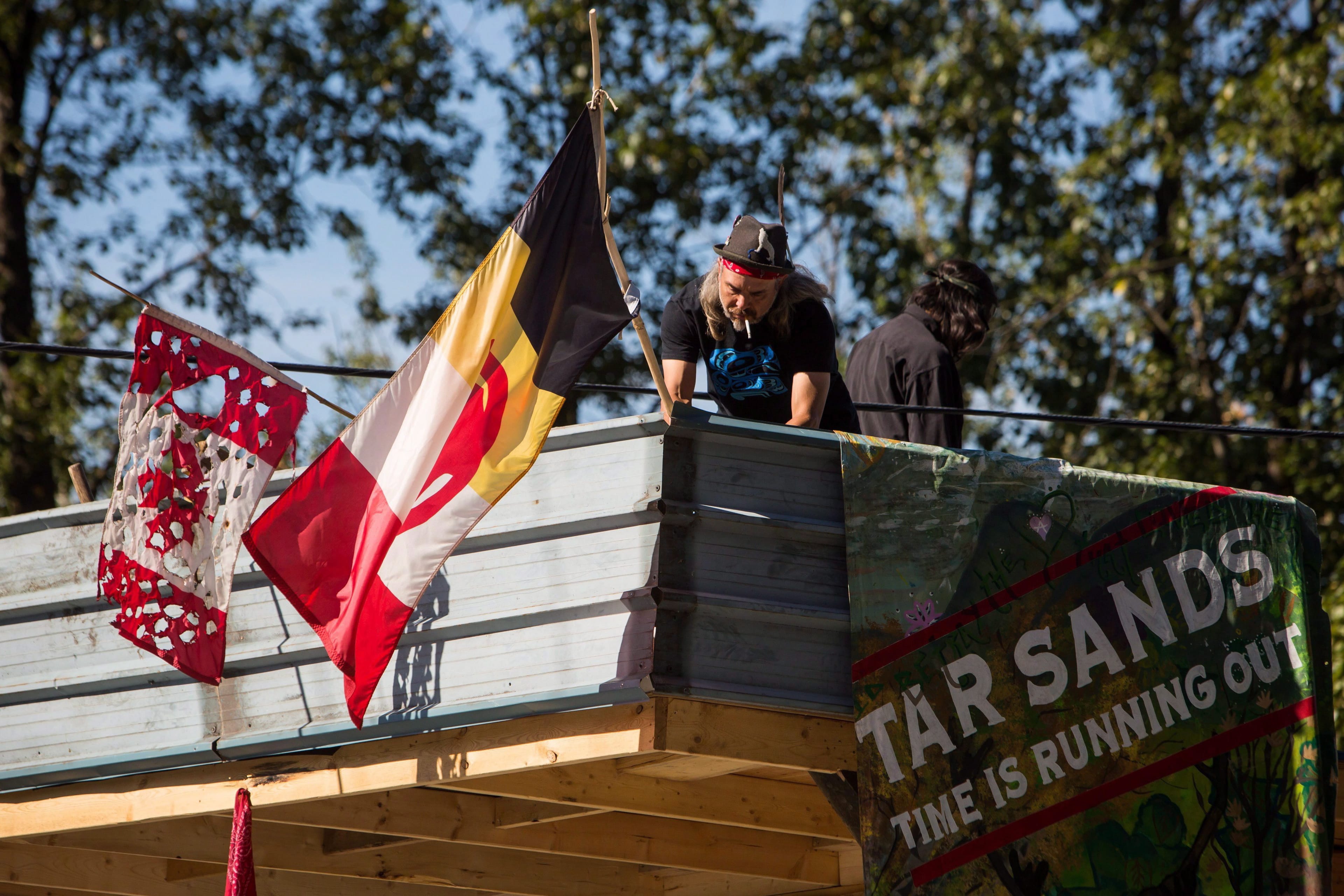 A man known as Blackwolf secures an American Indian Movement flag at Camp Cloud near the entrance of the Kinder Morgan Trans Mountain pipeline facility in Burnaby, B.C., on Saturday July 21, 2018. THE CANADIAN PRESS/Ben Nelms