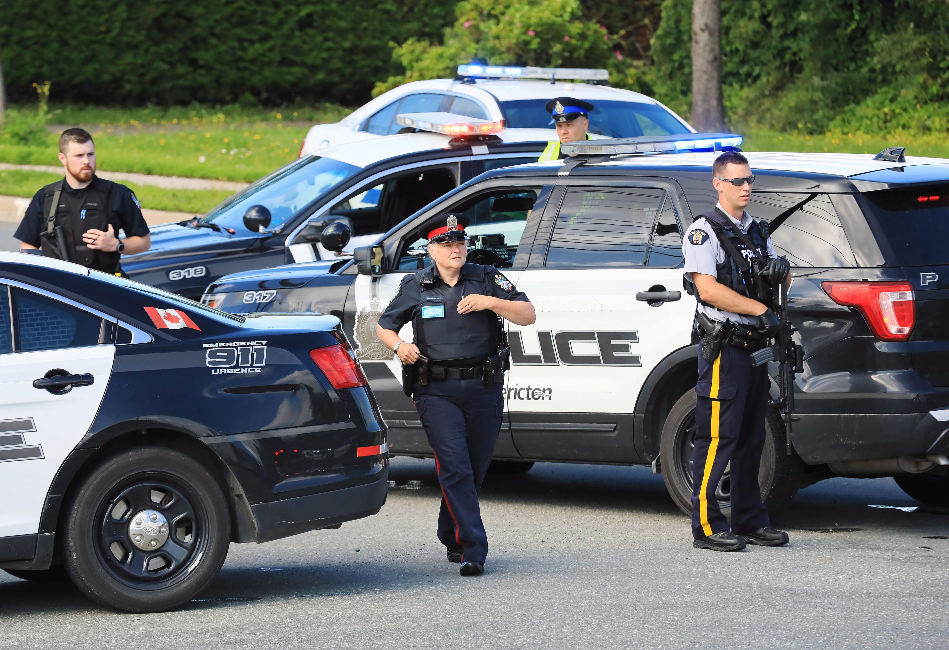 Police and RCMP officers survey the area of a shooting in Fredericton, N.B. on Friday, August 10, 2018. THE CANADIAN PRESS/Keith Minchin