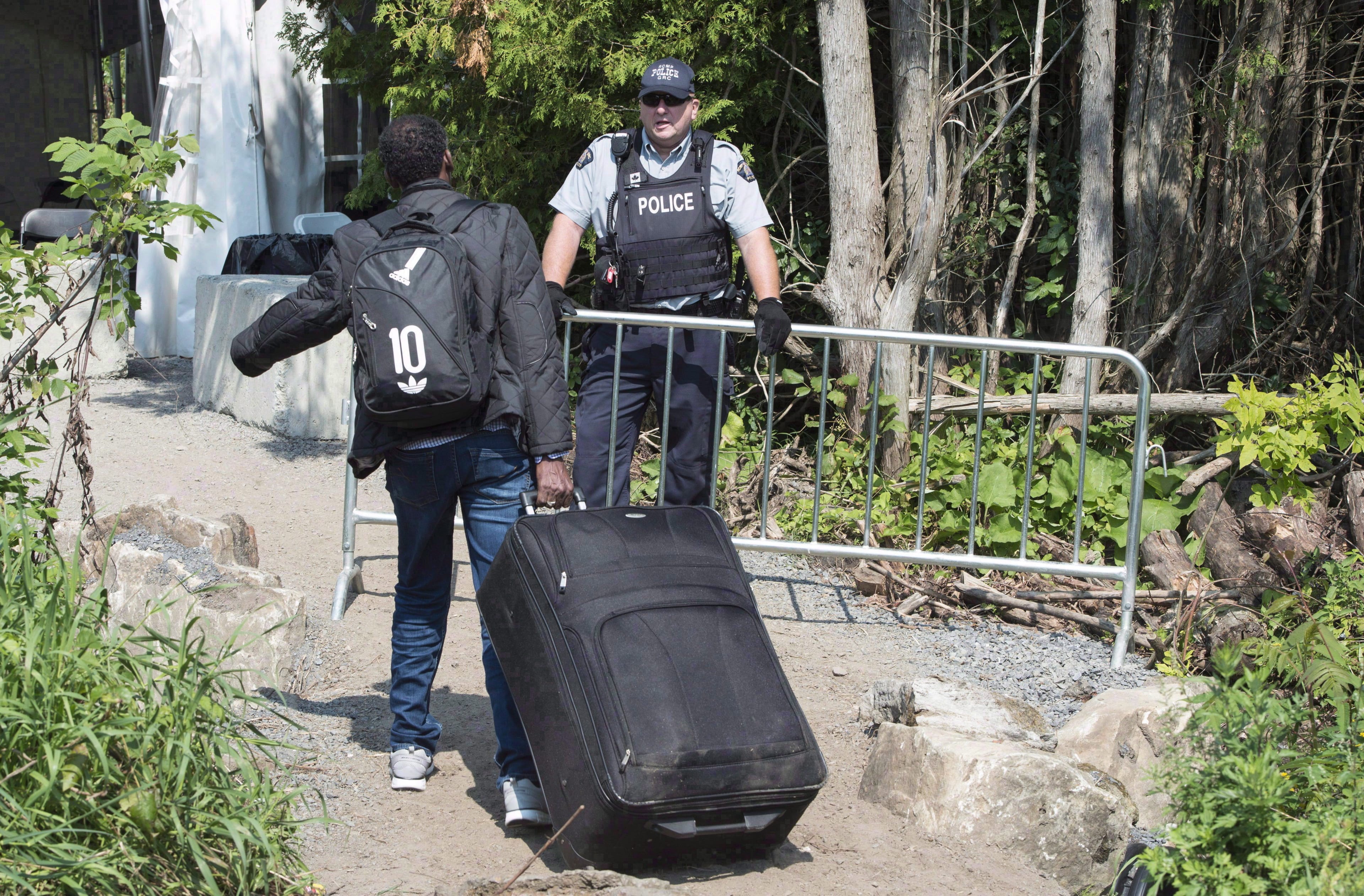 An asylum seeker is confronted by an RCMP officer as he crosses the border into Canada from the United States Monday, Aug. 21, 2017 near Champlain, N.Y. (THE CANADIAN PRESS/Paul Chiasson)