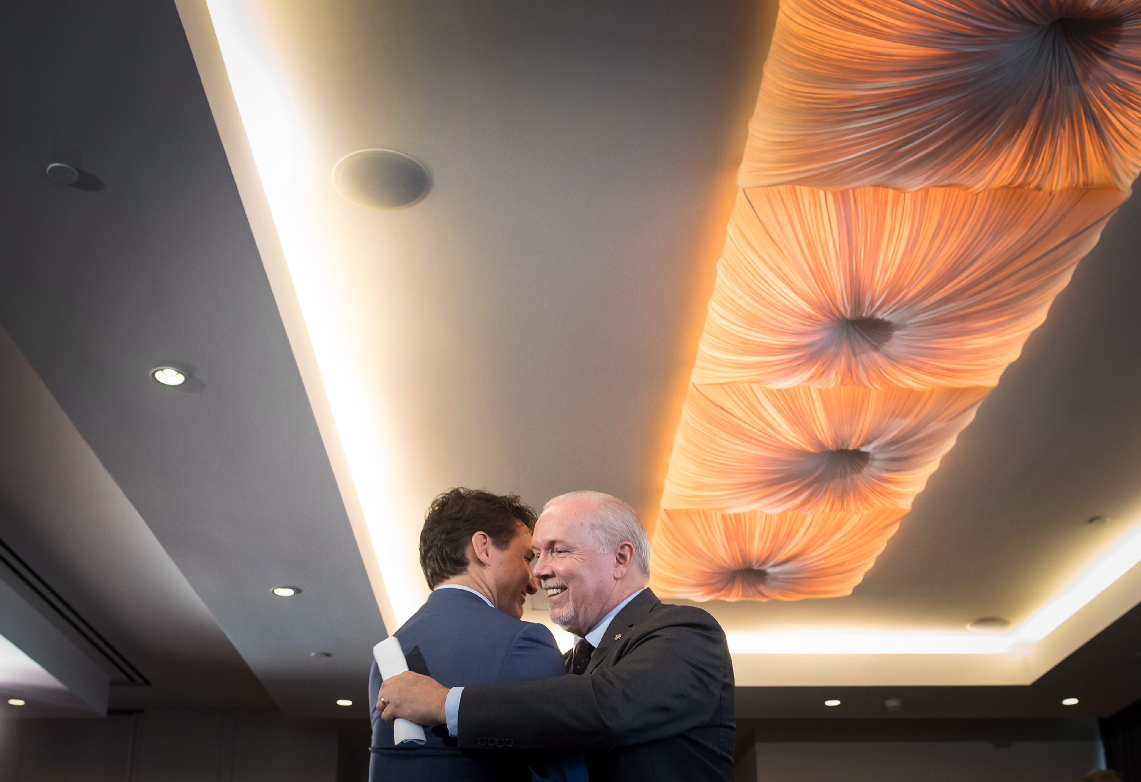 Prime Minister Justin Trudeau, left, and B.C. Premier John Horgan shake hands and embrace during an LNG Canada news conference in Vancouver on Tuesday, Oct. 2, 2018. LNG Canada announced that its joint venture participants Shell, PETRONAS, PetroChina, Mitsubishi Corporation and KOGAS made a final investment decision to build the LNG Canada export facility in Kitimat. (Darryl Dyck/CP)