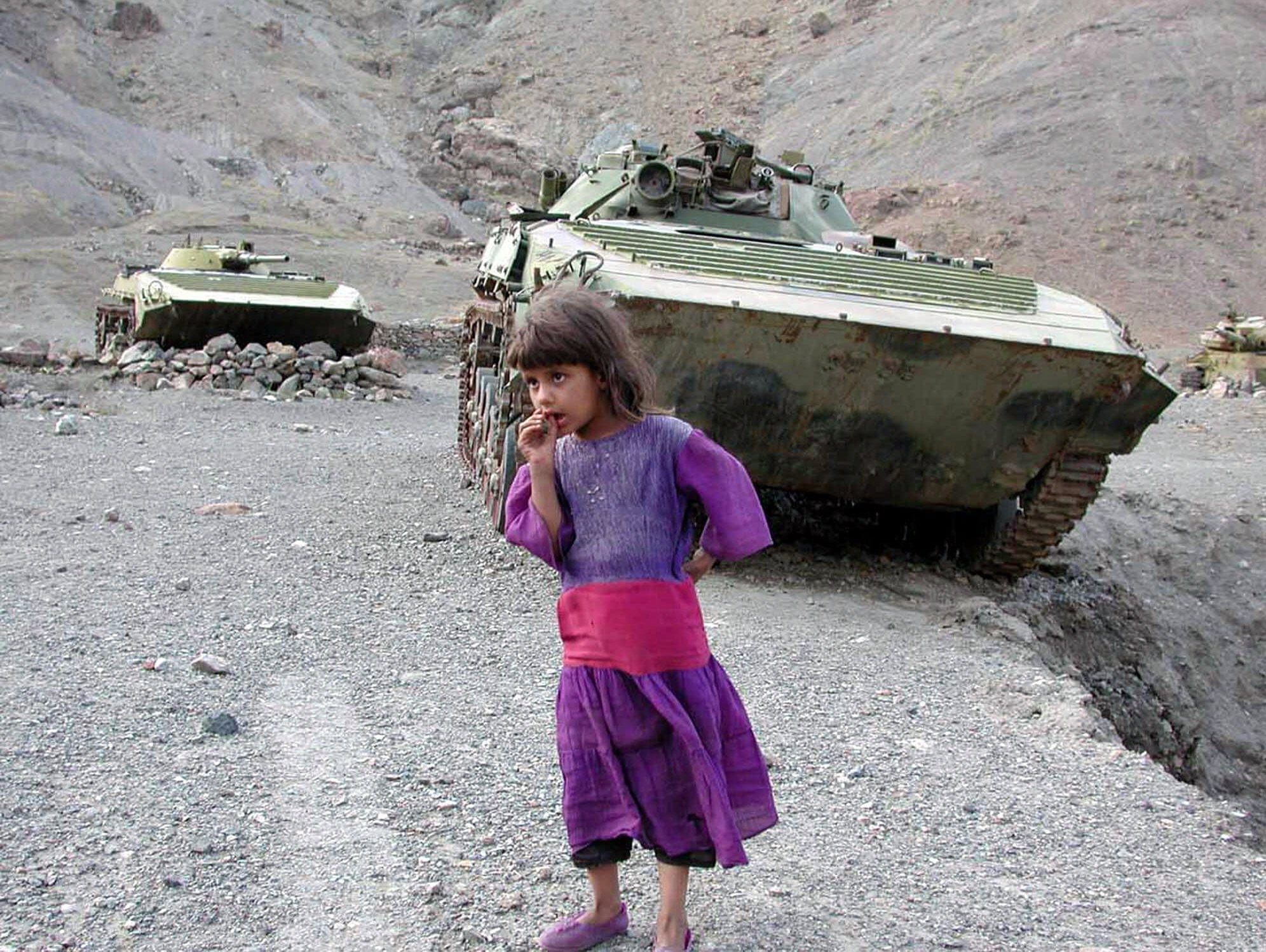 A girl stands before tanks the Soviet Army left north of Kabul in the 1980s. The image was taken 13 days after the Sept. 11, 2001 attacks (AP Photo/Alexander Merkushev, File)